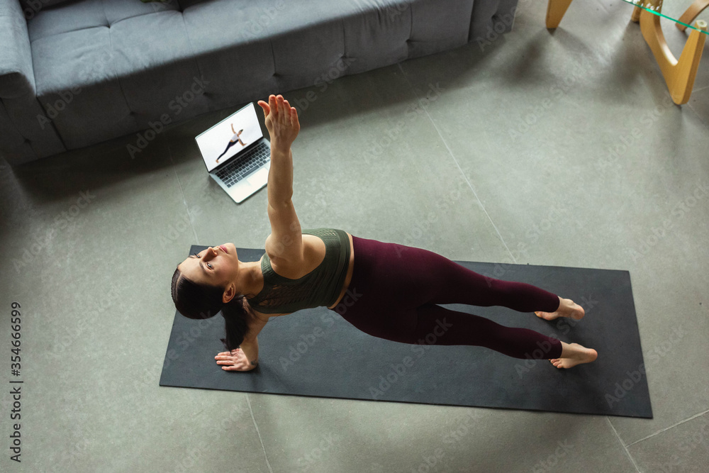 Fototapeta premium Meditation. Sporty beautiful young woman taking professional yoga lessons online and practice at home. Concept of healthy lifestyle, wellness, wellbeing, looking for new hobby. Flexible and motivated.