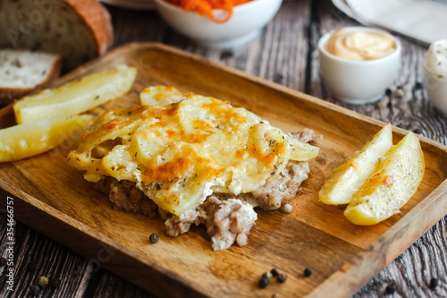 Tasty casserole with meat, potatoes, cheese and spices. Casserole served with carrot, bread and sour cream. Russian traditional dish. Dish on a wooden table