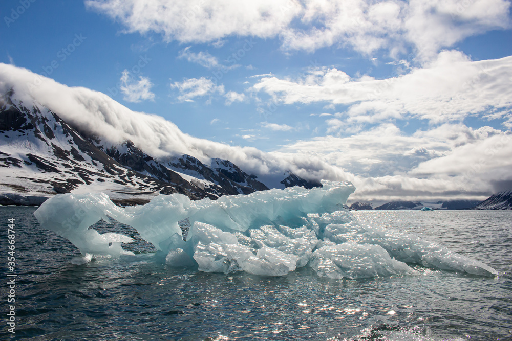 Fototapeta premium An Iceberg in the sea in front of Mountains in Svalbard
