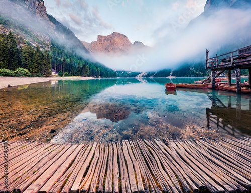 Foggy morning view of Braies (Pragser Wildsee) lake with old wooden pier. Picturesque summer scene of Fanes-Sennes-Braies national park, Dolomiti Alps, South Tyrol, Italy, Europe.