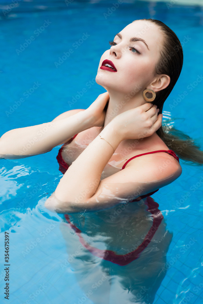 Beautiful young woman in red bikini refreshing at summer swimming pool