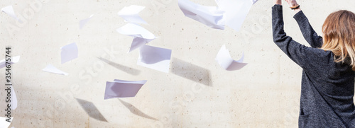 Woman throws a stack of white paper into the air tossing a wind burnout quitting giving up overwhelmed work paperless office chaos career haphazard concrete wall