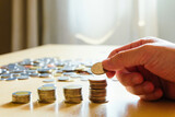 Selective focus Asian men hand put coin into stack. Saving plan for retirement planning, pension, tax reduction. Wealth and good financial or money investment concept.
