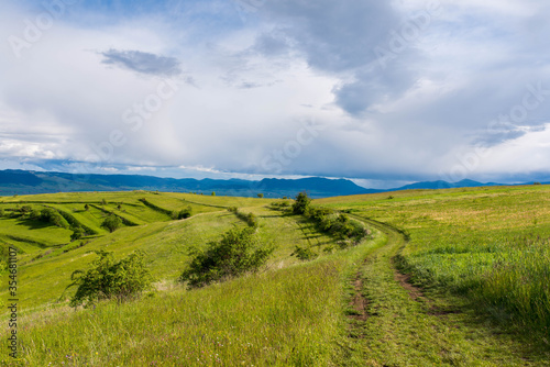 Gathering storm clouds over green hills , dirt road in the Carpathian mountains, Romania.