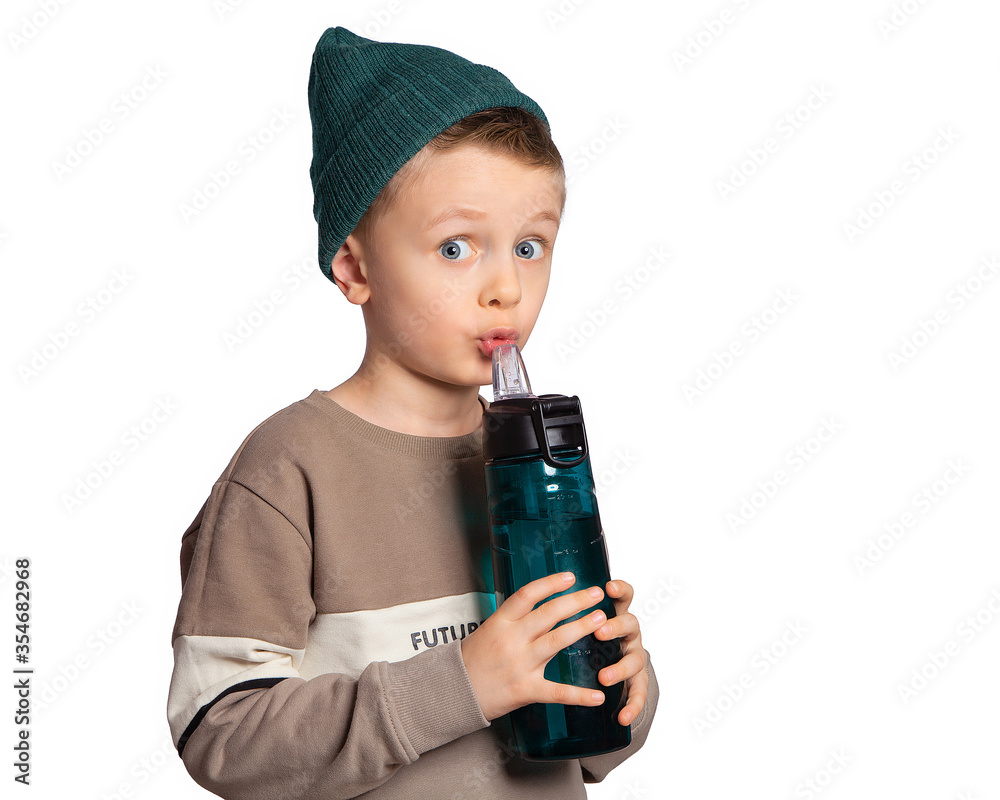 Beautiful European boy with a water bottle and sports drinks. The child drinks water from a bottle. Funny facial expression. Training, fitness, sports, physical education.