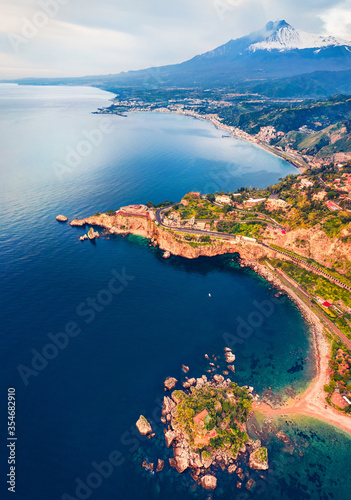 View from flying drone. Amazing morning view of Bella island and Etna volcano on background. Calm summser seascape of Mediterranean sea. Aerial view of Taormina town, Sicily, Itale, Europe.