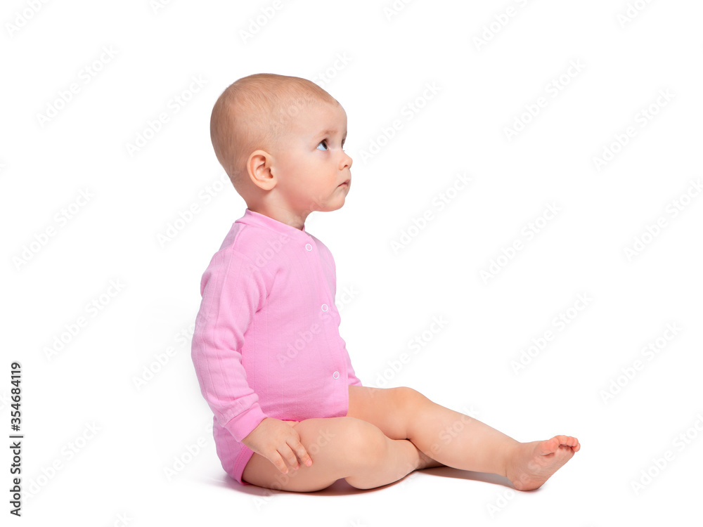 The baby sits sideways on a white background and looks up carefully. Baby girl in pink. Beautiful children, pretty girl. The baby sits sideways on a white background and looks up carefully. Baby girl in pink. Beautiful children, pretty girl.