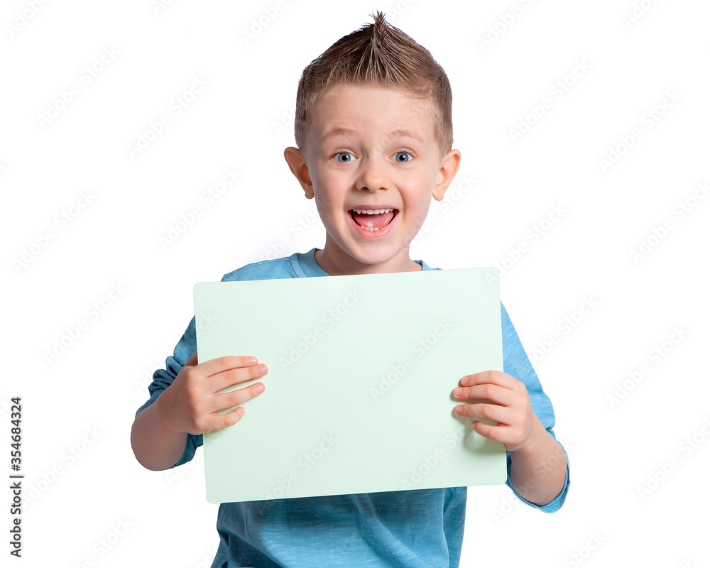 A beautiful boy holding a white sheet of paper, a white sign on a white background, laughing and smiling. The look of a child's blue eyes. Funny baby face. A beautiful boy holding a white sheet of paper, a white sign on a white background, laughing and smiling. The look of a child's blue eyes. Funny baby face.
