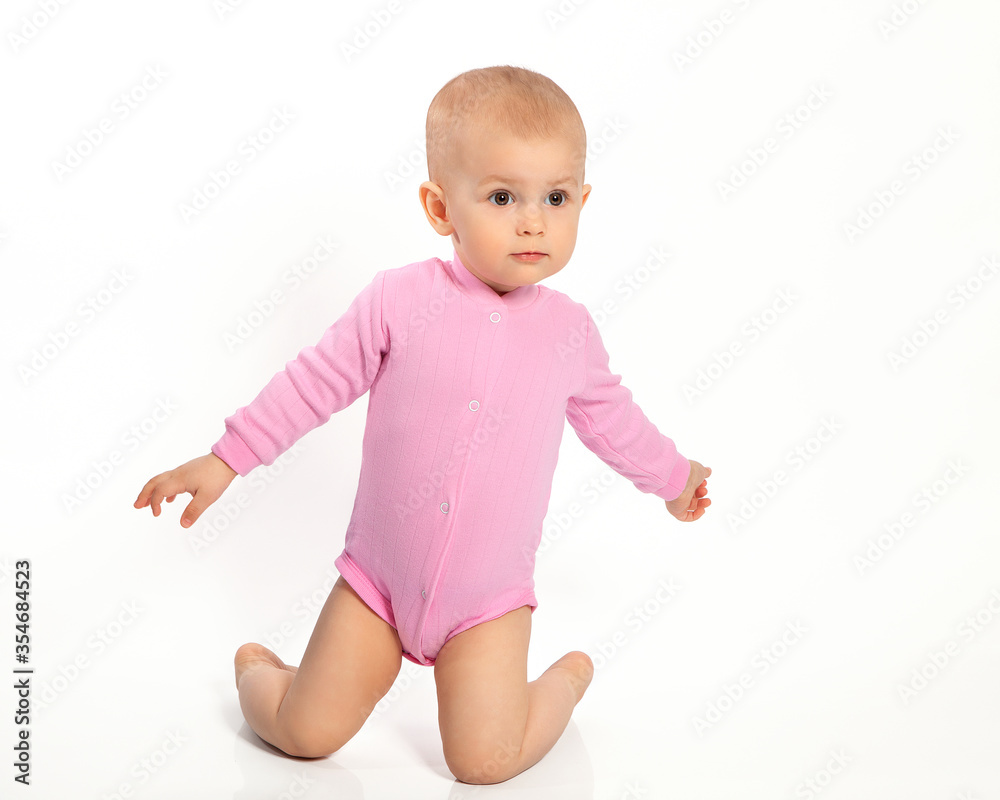 A little European girl baby is on her knees and spread her arms on a white background. Portrait of a cute little girl, a happy child. A little European girl baby is on her knees and spread her arms on a white background. Portrait of a cute little girl, a happy child.