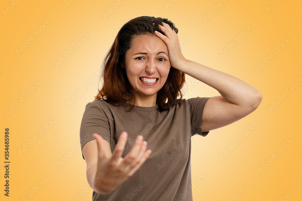 Portrait of an angry young Caucasian woman with tense hands, clutching her head. Yellow background. Human emotions, the concept of facial expression Portrait of an angry young Caucasian woman with tense hands, clutching her head. Yellow background. Human emotions, the concept of facial expression
