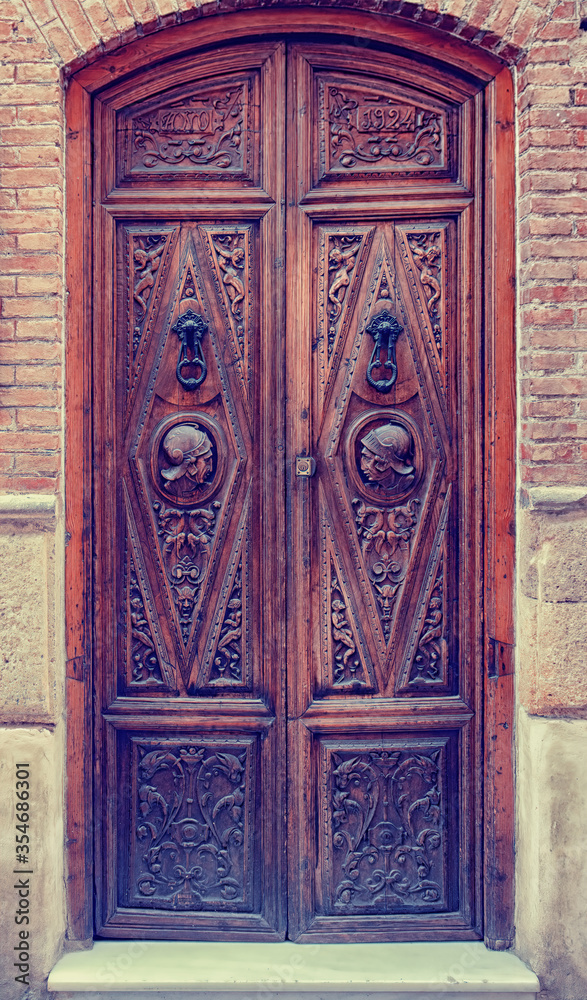 An ornately carved and decorated dark wooden door with two busts in military helmets and two metal door knockers of a residential property in the old quarter of Granada, Southern Spain