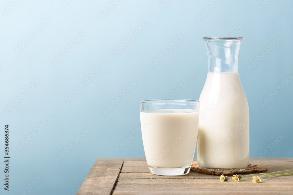 A glass and bottle of milk on wooden table with light blue background.