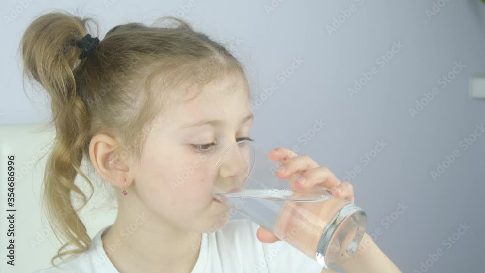 Caucasian girl child drinking water from a kitchen glass to stay hydrated during virus quarantine pandemic. Drink much water. Stay at home Caucasian girl child drinking water from a kitchen glass to stay hydrated during virus quarantine pandemic. Drink much water. Stay at home
