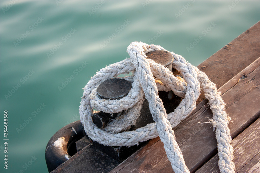 A black bollard on a wooden pier is wrapped in a mooring rope. Side view. Knecht is a pair of cast-iron pedestals. Knecht for mooring and securing mooring cables.