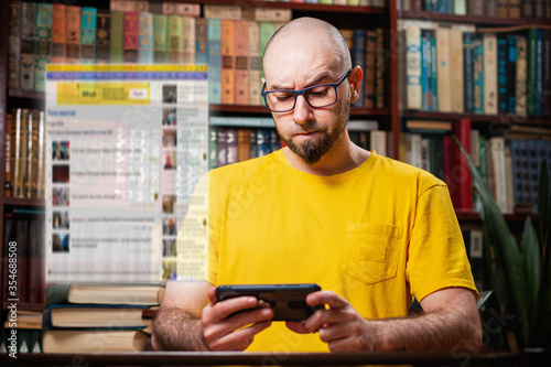 A bearded bald man with glasses uses a smartphone with a frown. Digital transparent window above the phone. The concept of a social network, distance learning, and self-isolation