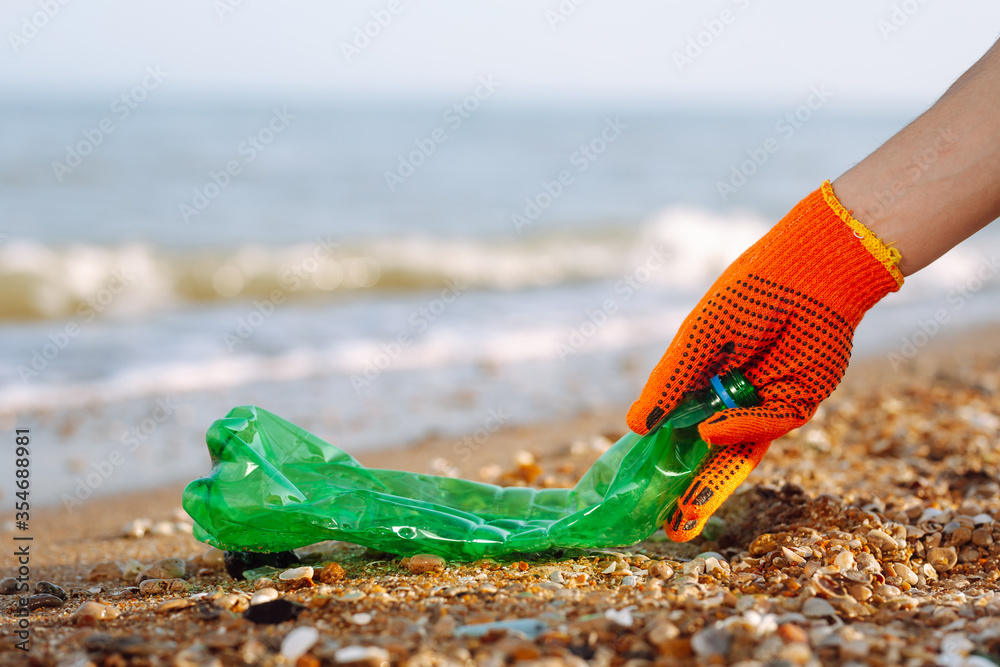 Closeup of young male volunteer's hands picks up plastic garbage on the ocean coast. A man collects waste on the seaside to save ecology and protect environment. Recycle litter and pollution concept.