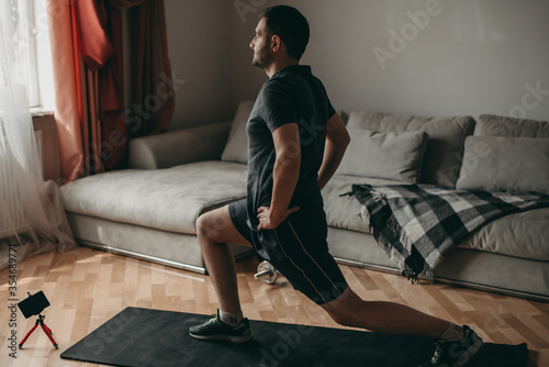 beautiful man doing squatting and lunges exercises with dumbbells on a ground pad, mat. Sport in quarantine at home.