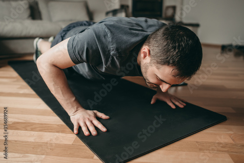 beautiful man doing plank and push-ups exercises with dumbbells on a mat. Sport in quarantine at home. Online lessons. Workout with an application on a smartphone.