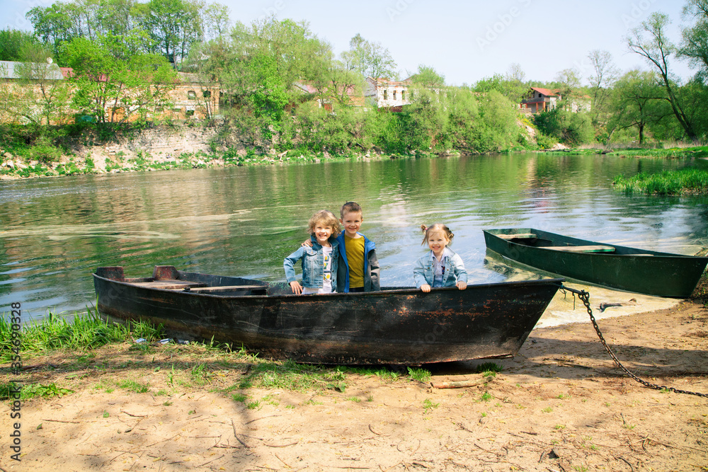 Obraz premium Three children in a boat on the river Bank are smiling, going to play fishermen and pirates. Family outdoor activities, Hiking, Hiking, camping. A happy family with three children.