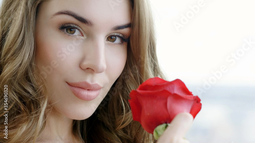 Portrait of an attractive blonde young woman with red rose looking at camera.