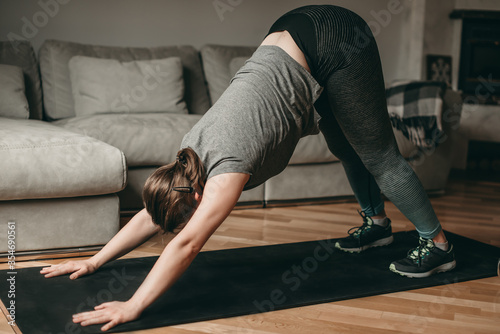 Young beautiful white woman doing stretching exercises on a ground pad, mat in leggings and top. Sport in quarantine at home.