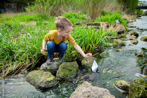 A European boy launches a paper boat in a stream. Children's games by the water. Safety of children in reservoirs.