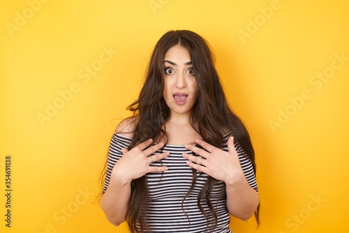 Shocked scared beautiful young woman keeps hands on chest, mouth widely opened, stares at camera realizes that she forgot to pay bills, receives big fine, isolated outdoors. Girl saying: Who, me?