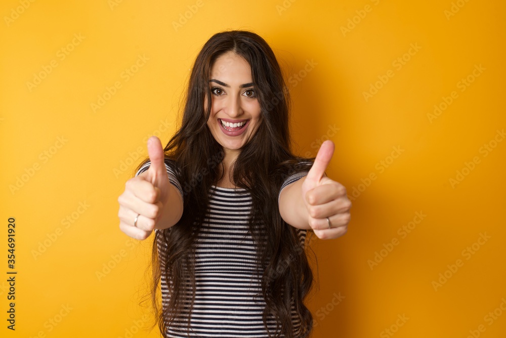 Good job! Portrait of a happy smiling blue eyed young successful woman giving two thumbs up gesture standing indoors. Positive human emotion facial expression body language. Funny girl