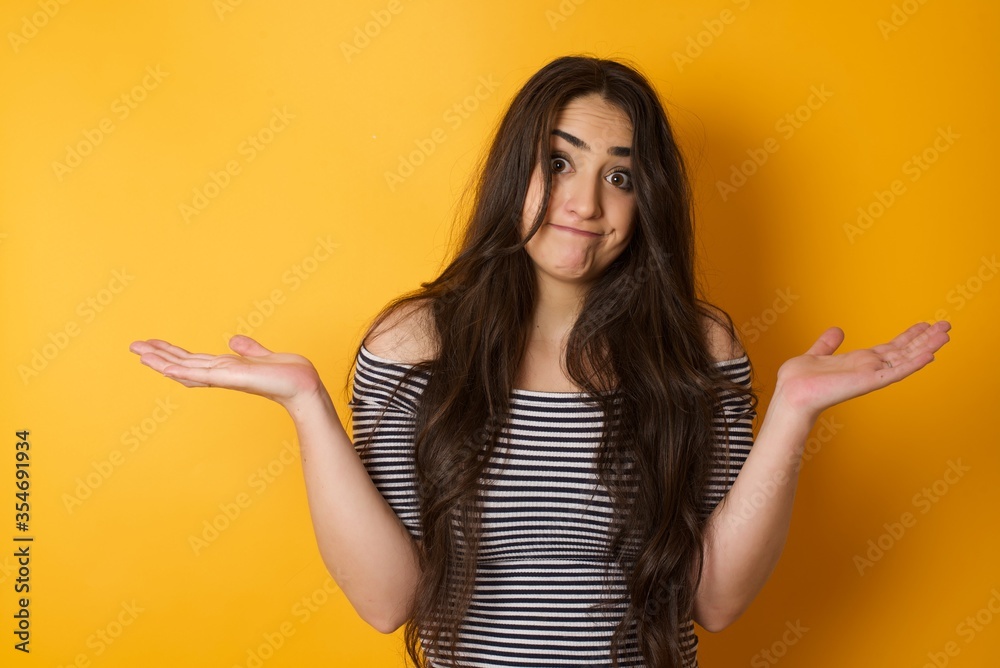 Puzzled and clueless young woman with arms out, shrugging her shoulders, saying: who cares, so what, I don't know. Negative human emotions, facial expressions, life perception and attitude.