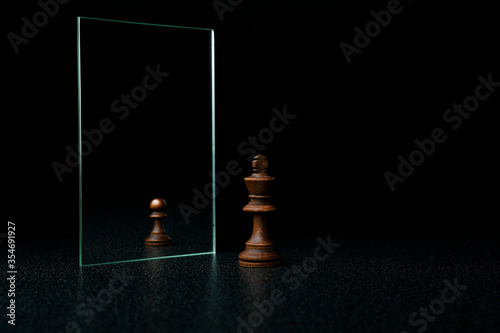 the king is reflected in the mirror as a pawn on black background. underestimation of their abilities photo