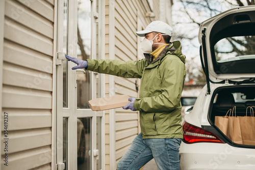 Deliveryman in a medical mask knocks to the door, delivers pizza to home from a restaurant. Quarantine, coronavirus.