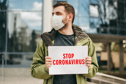 Young man in medical mask holding a tablet with the inscription stop coronavirus. Coronavirus isolation.