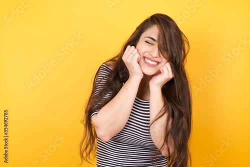 Slika na platnu Portrait of young cute european student being overwhelmed with emotions, expressing excitement and happiness with closed eyes and hands near face while smiling broadly over gray background