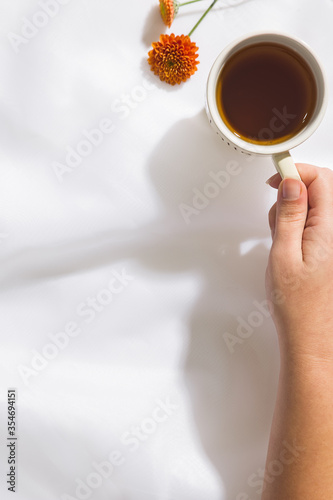 Top view of voile fabric background with female hand holding a mug of tea, two orange flowers, with space for text.