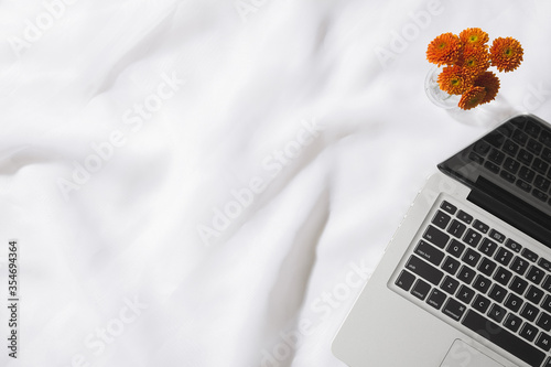 Top view of voile fabric background with a laptop, and a vase of orange flowers with space for text.