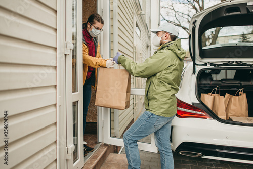 delivery man in a medical mask and gloves delivers the parcel in a craft package to the woman. Quarantine, coronavirus, isolation.