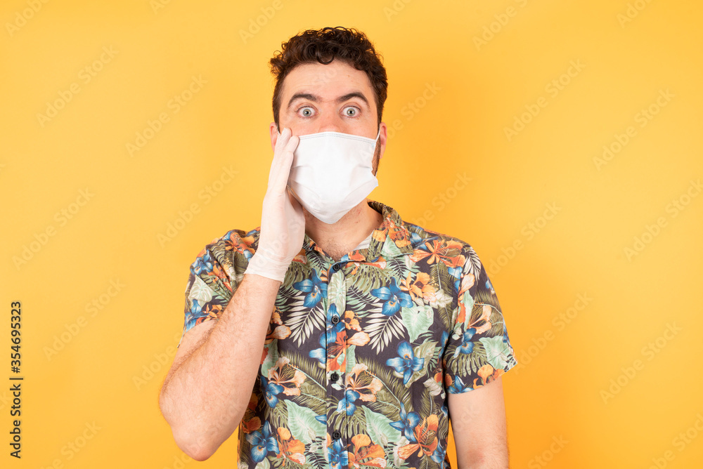 Horizontal portrait of shocked caucasian male wearing hawaiian shirt and medical mask looks with great surprisment being very stunned, astonished with unexpected news, Horizontal portrait of shocked caucasian male wearing hawaiian shirt and medical mask looks with great surprisment being very stunned, astonished with unexpected news,