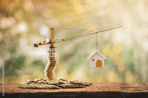Stacking gold coins with increase and tower crane and hoist brake solutions with build new house in the public park, saving money and loan for construction real estate and home concept.