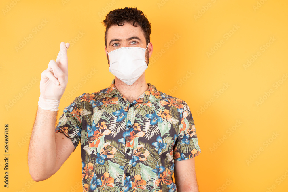 Young Cucasian businessman wearing hawaiian shirt and medical mask standing against yellow background pointing up with fingers number ten in Chinese sign language Shi Young Cucasian businessman wearing hawaiian shirt and medical mask standing against yellow background pointing up with fingers number ten in Chinese sign language Shi