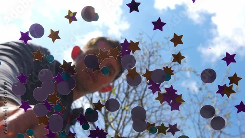 High quality close-up 4k slow motion video of a blurred man mixing with his pointing finger colorful large sparklers confetti on a glass top table, view from the bottom. Blue sky on a background. 