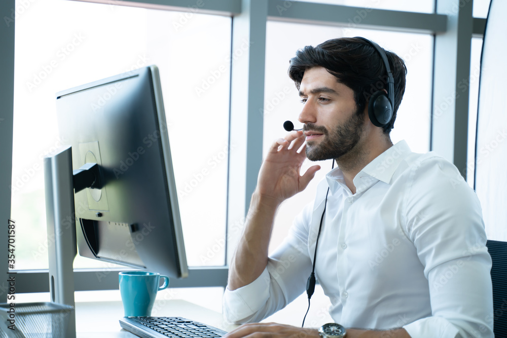 Smiling handsome young male call centre operator with headset.Confident male customer service representative,operator,agent,call centre worker,support staff speaking with head set in modern office - obrazy, fototapety, plakaty 