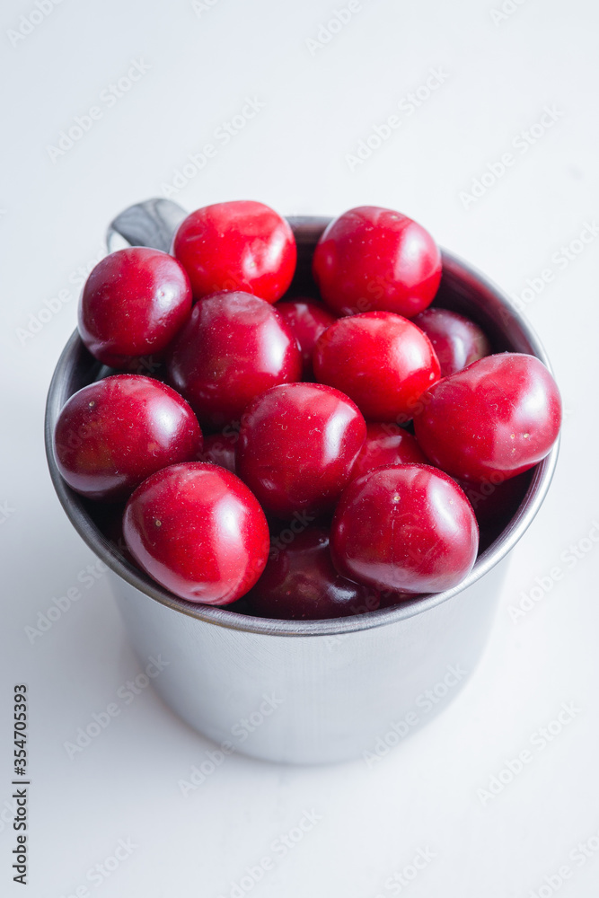 Sweet cherries in a steel mug on a white paper background Sweet cherries in a steel mug on a white paper background