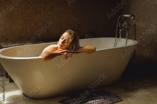 Beautiful smiling Caucasian woman posing with wet hair at bathroom, relaxing in the bath in the bathroom. young woman lying in bathtub. .woman taking a bath, personal care photo