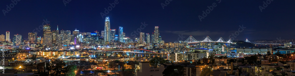 Fototapeta San Francisco skyline night panorama with city lights, the Bay Bridge and light trails on the highway