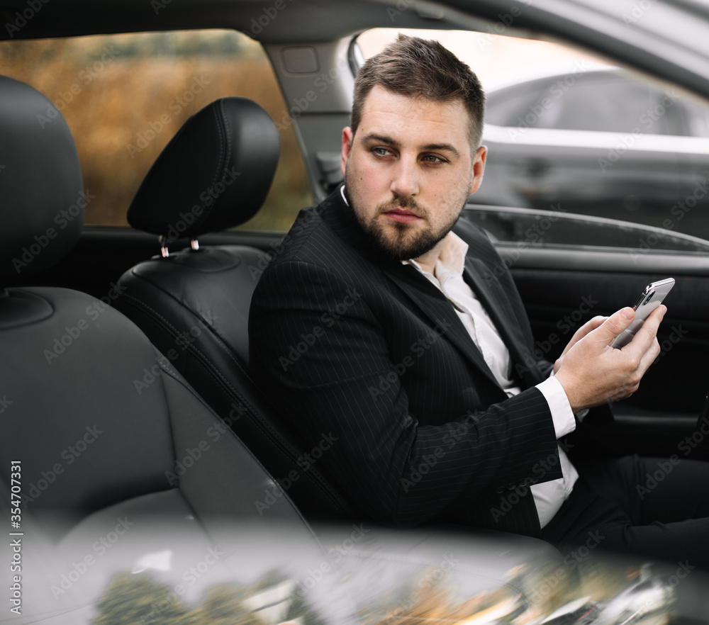 Handsome caucasian businessman driver inside in vehicle  with coffee and gadget and check mail and talking with partners