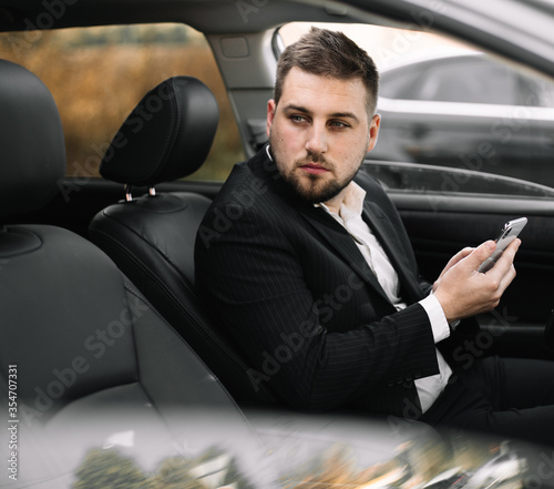 Handsome caucasian businessman driver inside in vehicle  with coffee and gadget and check mail and talking with partners © klepach