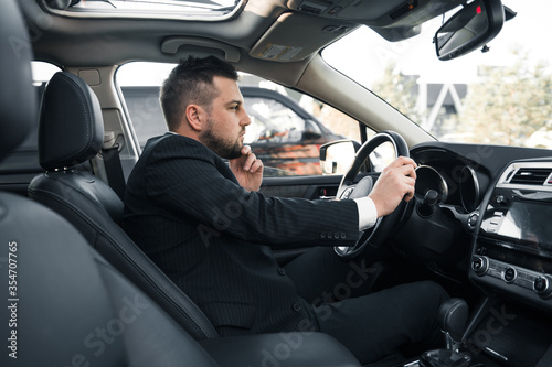 Handsome caucasian businessman driver inside in vehicle with coffee and gadget and check mail and talking with partners