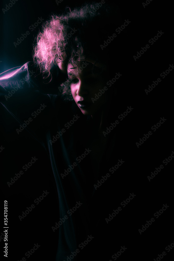 A creatively processed photo of a beautiful Afro-American girl with curly hair who poses in the studio on a dark background.