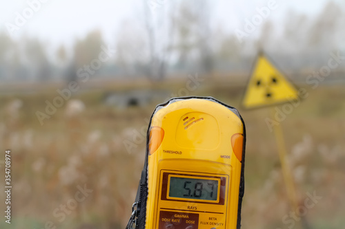 A dosimeter is held in front of a radioactivity warning sign, showing 5.87 millisieverts. Pripyat city, Chernobyl exclusion zone, Ukraine. photo