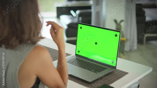 Girl sitting in living room opposite laptop with Green Mock Up Screen and talking with someone